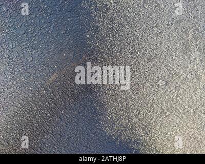 Frozen texture covered by a thin layer of snow. The sun shines and melts the frozen surface, the melted ice Stock Photo