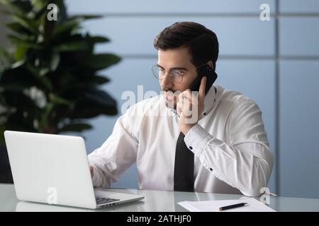 Businessman looks at computer screen talking on phone consult client Stock Photo