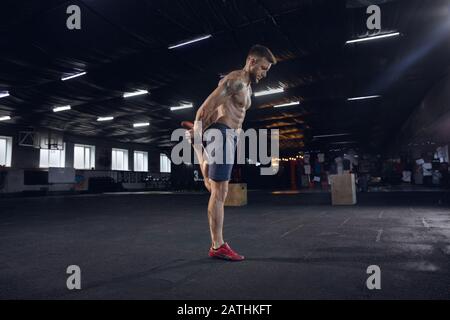 Young healthy man, athlete doing exercises, stretching in gym. Single caucasian model practicing hard, training his body. Concept of healthy lifestyle, sport, fitness, bodybuilding, wellbeing.