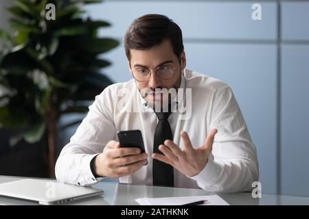 Angry businessman holding gadget feels annoyed with broken smartphone Stock Photo