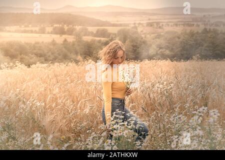 Young woman in a wheat field with daisies in her hands Stock Photo