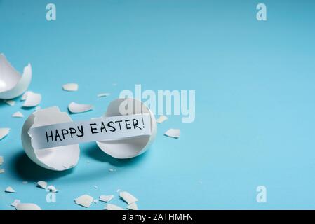 Cracked egg with text HAPPY EASTER on light blue background. Copy space Stock Photo