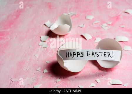 Cracked egg with text HAPPY EASTER on pink background. Copy space Stock Photo