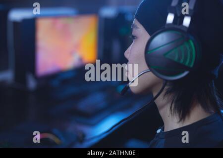 Side view close up of young Asian man playing videogames and wearing headphones in dark cyber like interior, copy space Stock Photo