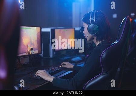 Side view portrait of young Asian man playing videogames and wearing headphones in dark cyber interior, copy space Stock Photo
