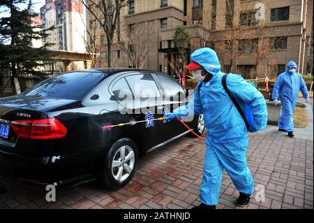 A Chinese medical worker wearing protective clothing and face mask disinfects a car in front of a residential building isolated for prevention of the Stock Photo