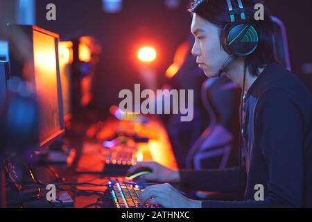 Side view portrait of young Asian man playing video game in dark room, focus on male hands on brightly lit keyboard, copy space Stock Photo