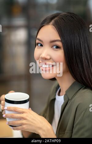 Long-haired brunette asian girl sitting and having coffee Stock Photo