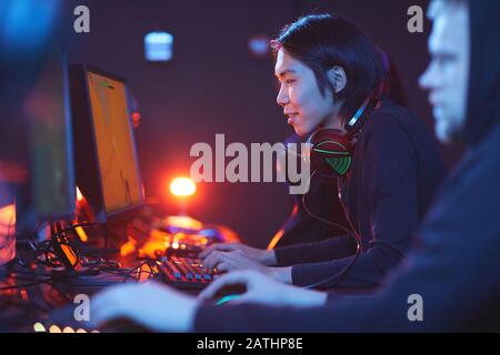 Side view portrait of smiling Asian man playing video games with pro cyber sport team, copy space Stock Photo