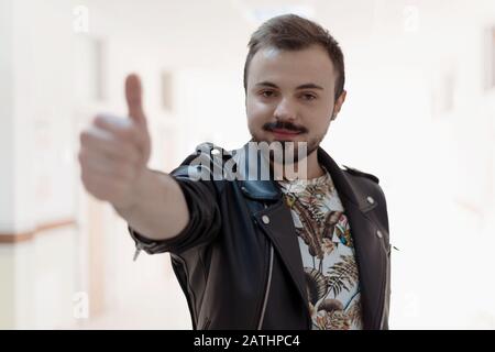 Portrait of smiling, bearded man gesturing thumb up in corridor or hall university. Concept approving, recommend, like new product. Stock Photo