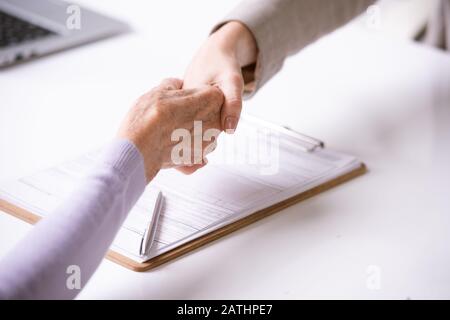 Close-up of advisor making handshake with retired woman after signing document Stock Photo