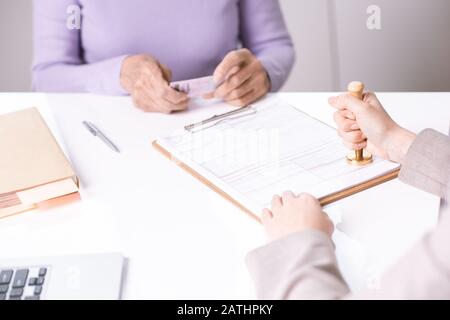 Close-up of unrecognizable specialist stamping paper while certifying it for senior lady Stock Photo