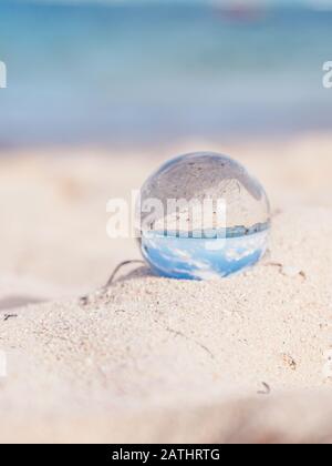 Glass round ball on the beach reflects the sea in summer at sunset ...