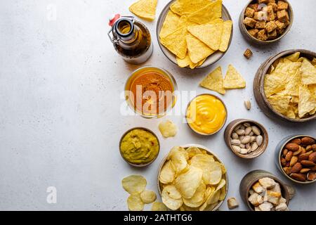 Veraity bowls of beer snacks and sauces on stone table. Nuts, chips, nachos, crackers. Top view with copyspace Stock Photo