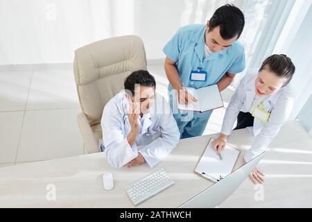 Group of multi-ethnic medical specialists watching online webinar, taking notes and answering questions on teacher Stock Photo