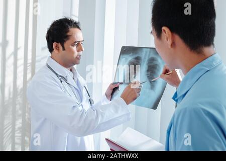 Serious doctor showing lungs x-ray to coworker and discussing possible case of coronavirus or pneumonia Stock Photo