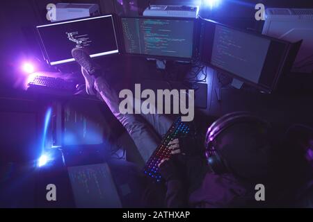 Top view at young man surrounded by multiple screens programming or hacking security in dark room, copy space Stock Photo
