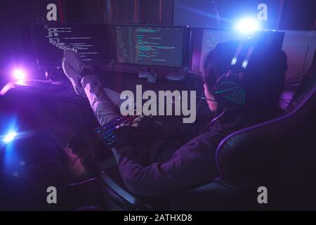 Back view at young man surrounded by multiple screens programming or hacking security in dark room, copy space Stock Photo