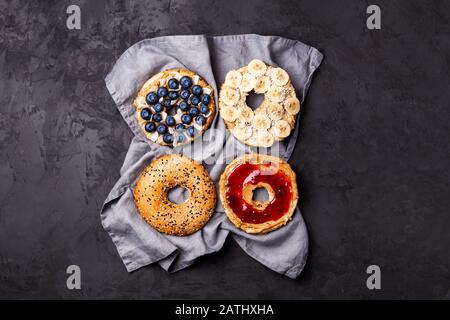 Variety of bagels with different toppings and natural paleo nut peanut cashew creamy butter on dark gray background.Healthy breakfast brunch concept Stock Photo