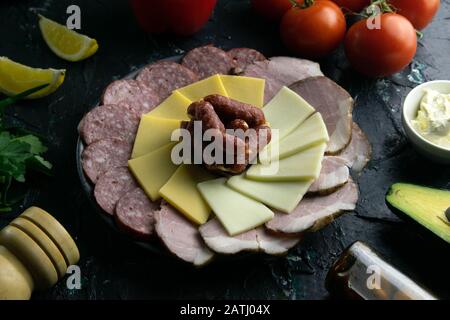 Grey plate with sausages around the salami, ham, cheese and mozzarella. Tomato, souce, olives, lemon, olive oil with spice Stock Photo