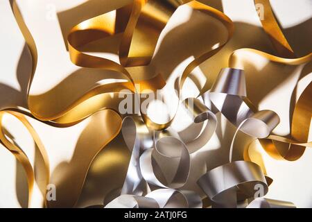 Gold and silver curl ribbon on white background in hard light with shadows. Stock Photo