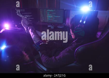 Back view at young man surrounded by multiple screens programming or hacking security in dark room, copy space Stock Photo
