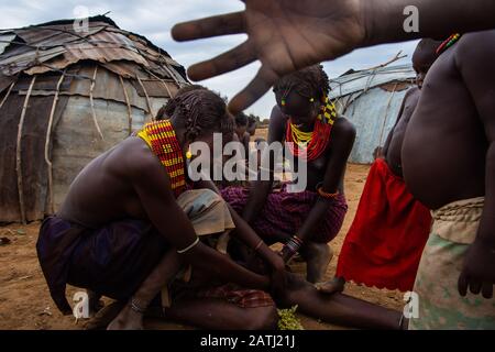 Omorate, Ethiopia - Nov 2018: Woman of Dassanech tribe with kids picking sorghum in front of the tribal house. Omo valley Stock Photo