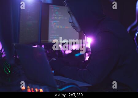 Side view at unrecognizable cyber security hacker wearing hood while working on programming in dark room, copy space Stock Photo