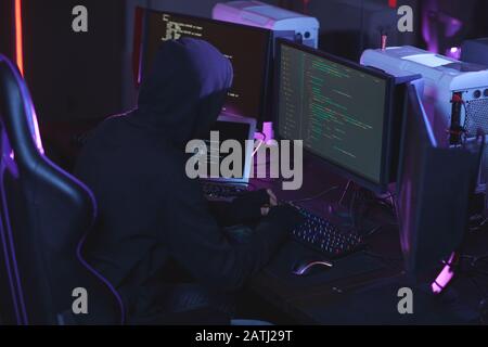 High angle view at unrecognizable cyber security hacker wearing hood while working on programming code in dark room, copy space Stock Photo