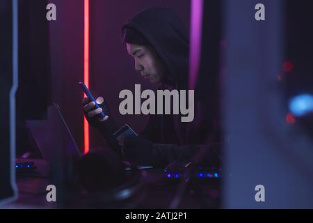 Side view portrait of Asian man wearing black and using computer while hacking credit card, cyber security concept, copy space Stock Photo