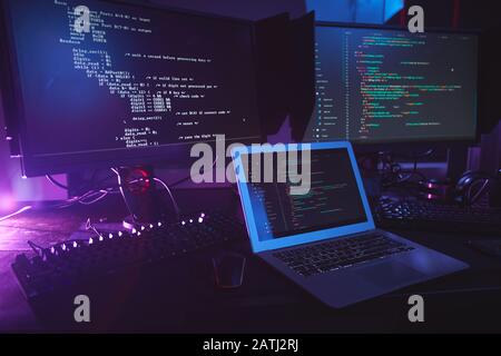 Background image of various computer equipment with programming code on screens on table in dark room, cyber security concept, copy space Stock Photo