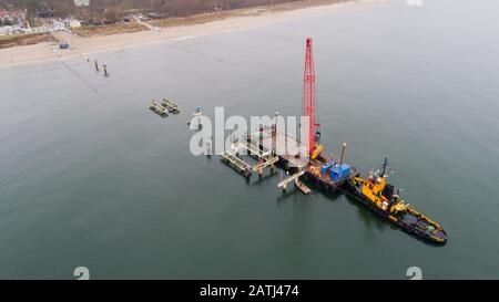 03 February 2020, Mecklenburg-Western Pomerania, Koserow: A mobile crane is used to dismantle the sea bridge built in 1993 in the Baltic resort of Koserow (aerial photo with a drone). A new pier is to be built by August 2020. It should also rise about 280 metres into the sea, but look completely different from other sea bridges from the Baltic Sea and be barrier-free. According to the plans, the special features are, in addition to a wave appearance in the top view, an almost square bridgehead with a bell tower. The new building is to cost 7.4 million euros. The construction is financed with t Stock Photo