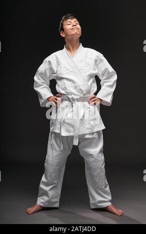 a teenager dressed in martial arts clothing poses on a dark gray background, a sports concept Stock Photo