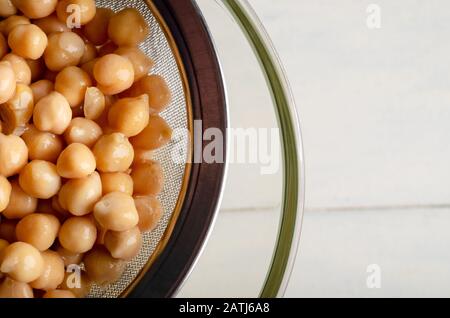 Overhead shot of chickpeas being strained through a metal sieve into a glass bowl to release aquafaba. Copy space to right. Stock Photo