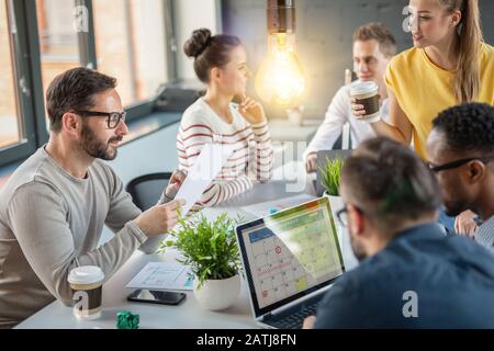 Young business people are discussing together a new startup project. A glowing light bulb as a new idea. Stock Photo