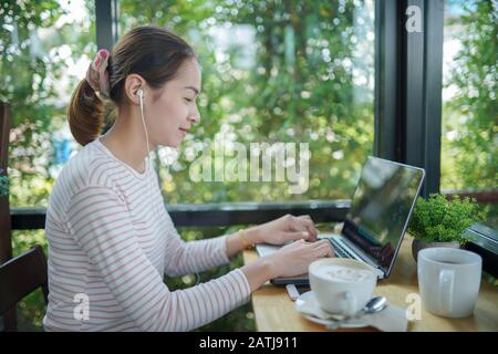 Young woman freelance use a laptop and headphone editing video footage in the coffee shop this is the lifestyle of the content creator Stock Photo