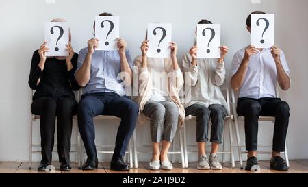 Diverse employees hold sheets with question marks wait for interview Stock Photo