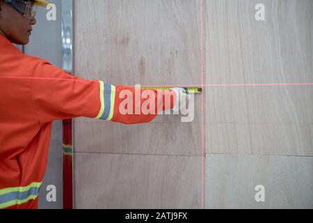 Carpenter uses a tape measure to measure the area in the vertical level with a laser machine. Stock Photo