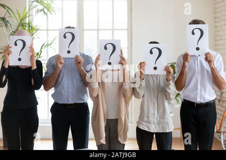 Diverse employees hide faces holding sheets with question marks Stock Photo