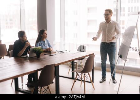 Businessman doing presentation, using whiteboard, explaining to colleagues Stock Photo