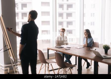 Businessman doing presentation, using whiteboard, explaining to colleagues Stock Photo