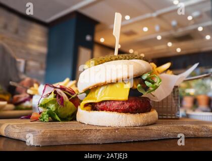 Melted cheese on a portobello mushroom and beetroot and bean vegetarian burger in a bun, on a wooden serving board, with a side salad and metal basket Stock Photo