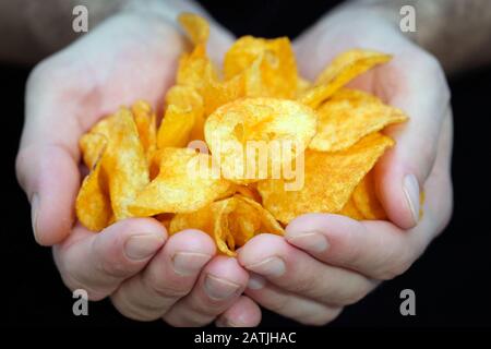 The guy holds potato chips in his hands. Hands with chips close-up. Harmful junk food for health. Potato snacks for beer. Stock Photo