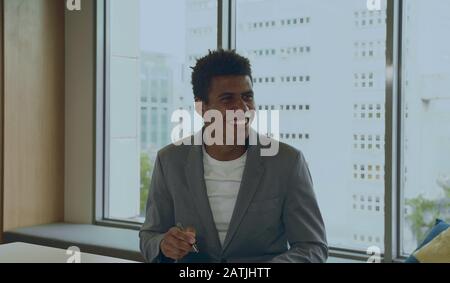 Cheerful elegant African-American man in suit with pen smiling while communicating with coworkers in office Stock Photo