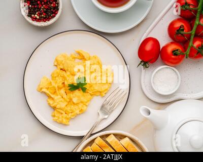 Scrambled eggs, Omelette. Breakfast with pan-fried eggs, cup of tea, tomatoes on white stone marble background. Top view Stock Photo