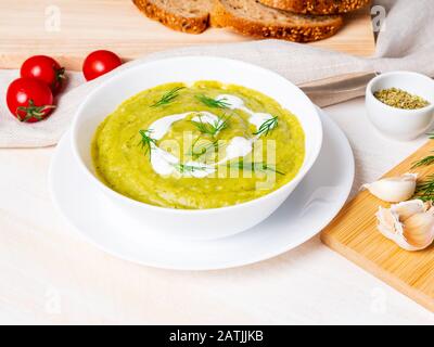 large white bowl with vegetable green cream soup of broccoli, zucchini, green peas on white background, side view Stock Photo