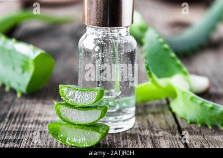 A slice of aloe vera and green leaves with aloe vera essential oil on a wooden table. Skin care products. Stock Photo