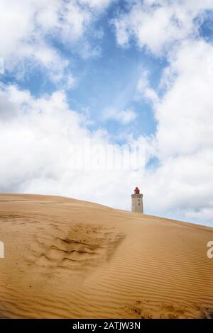 Lighthouse rising up behind a sand dune under a blue heaven with fluffy white clouds Stock Photo