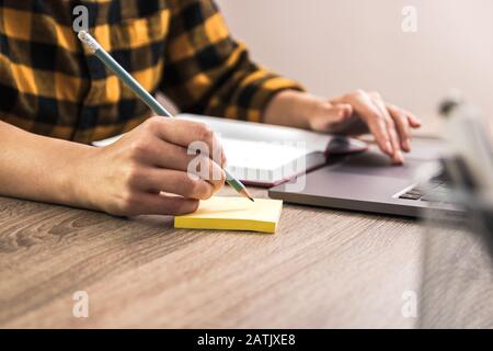 quick note. close up hands of a businesswoman, student or freelancer in yellow shirt making a note on sticky note Stock Photo