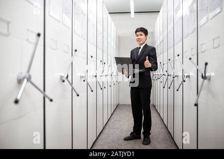 Business man, bank manager using notebook in a locker server room, safe deposit boxes with vault door. Stock Photo